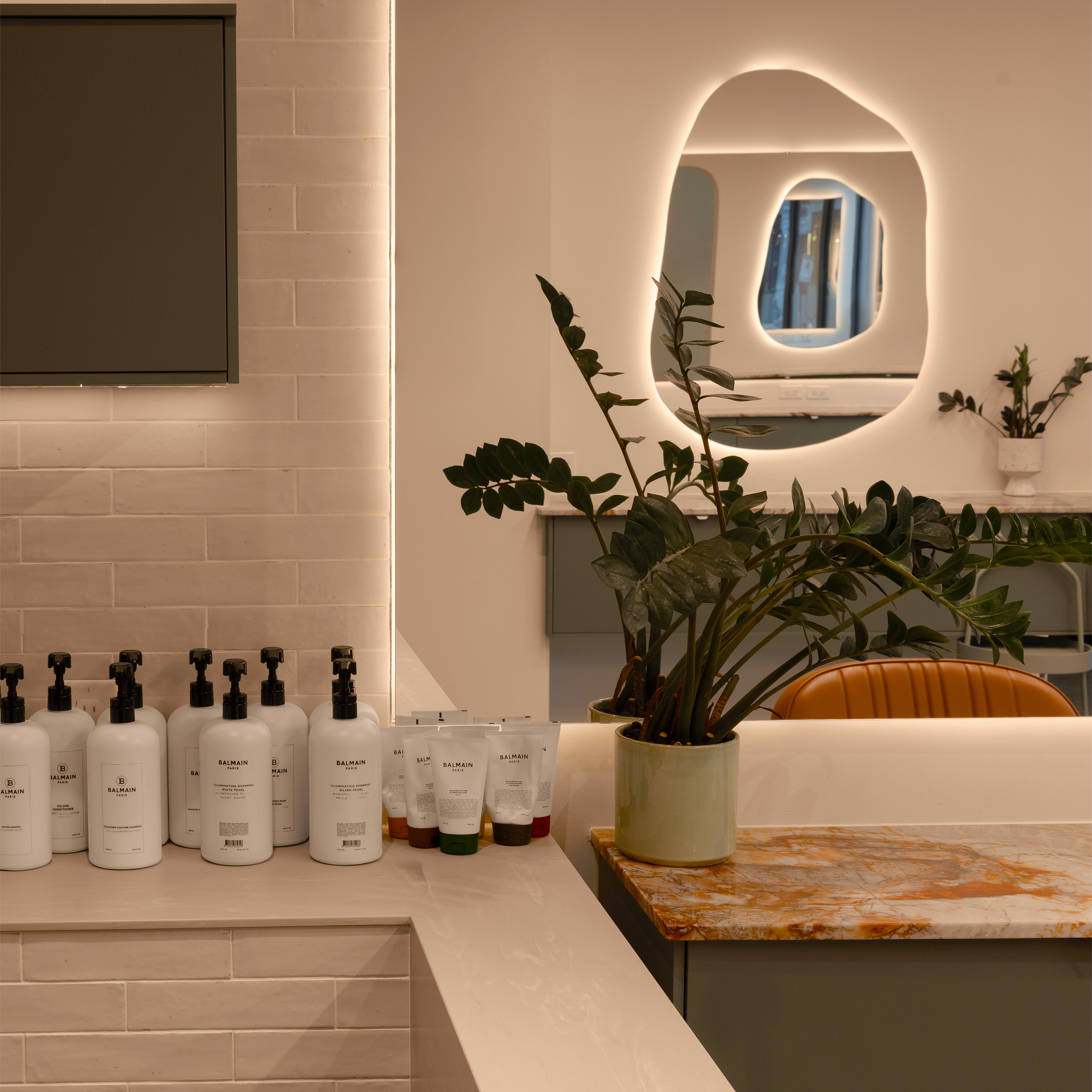 Salon interior with backbar products, a plant, and a mirror with a circular light fixture.