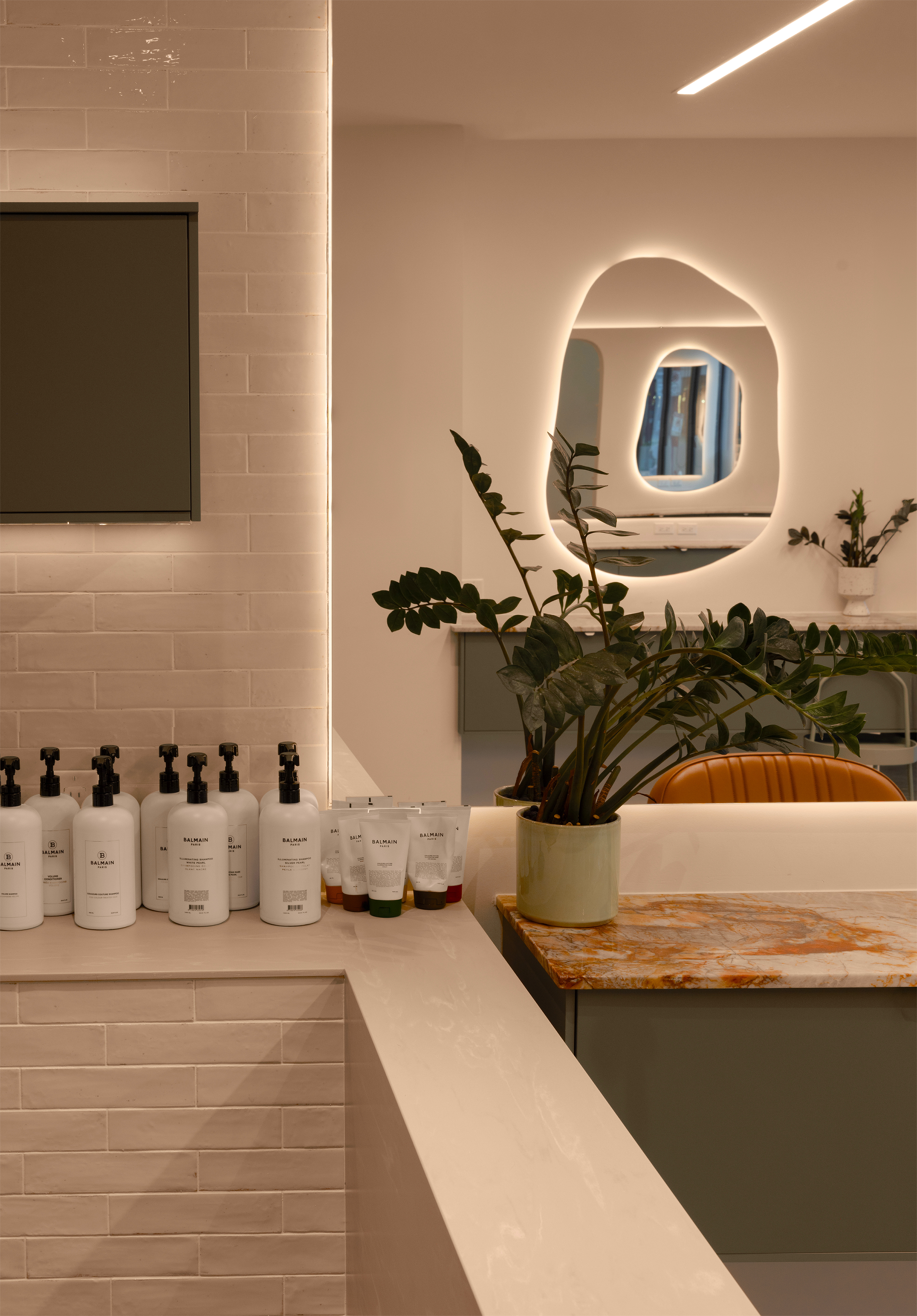 Salon interior with backbar products, a plant, and a mirror with a circular light fixture.