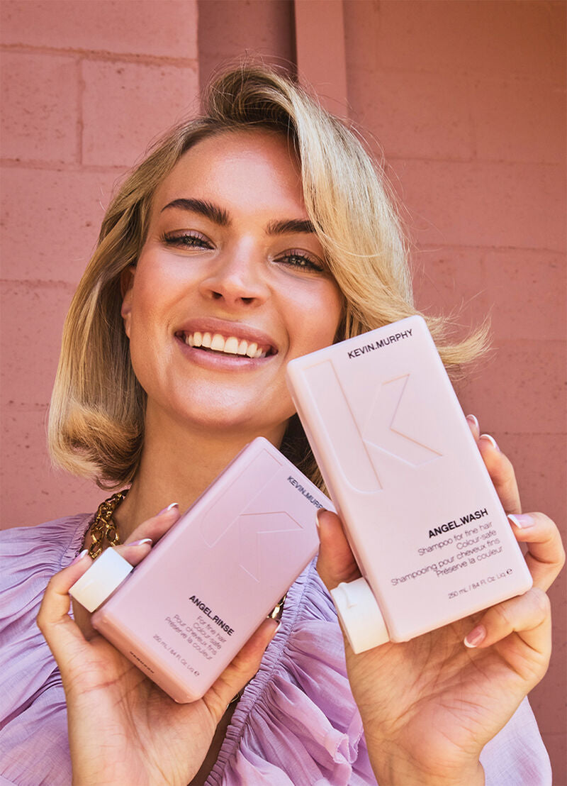 Woman holding Kevin Murphy hair products against a pink brick wall