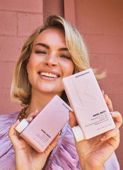 Woman holding Kevin Murphy hair products against a pink brick wall