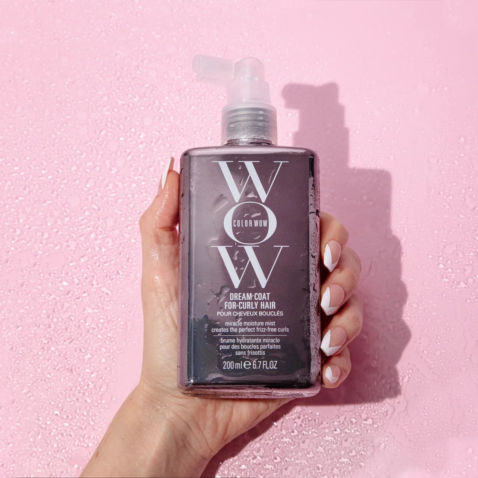Hand holding a bottle of WOW Color Wow hair product against a pink background