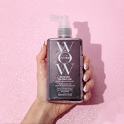 Hand holding a bottle of WOW Color Wow hair product against a pink background