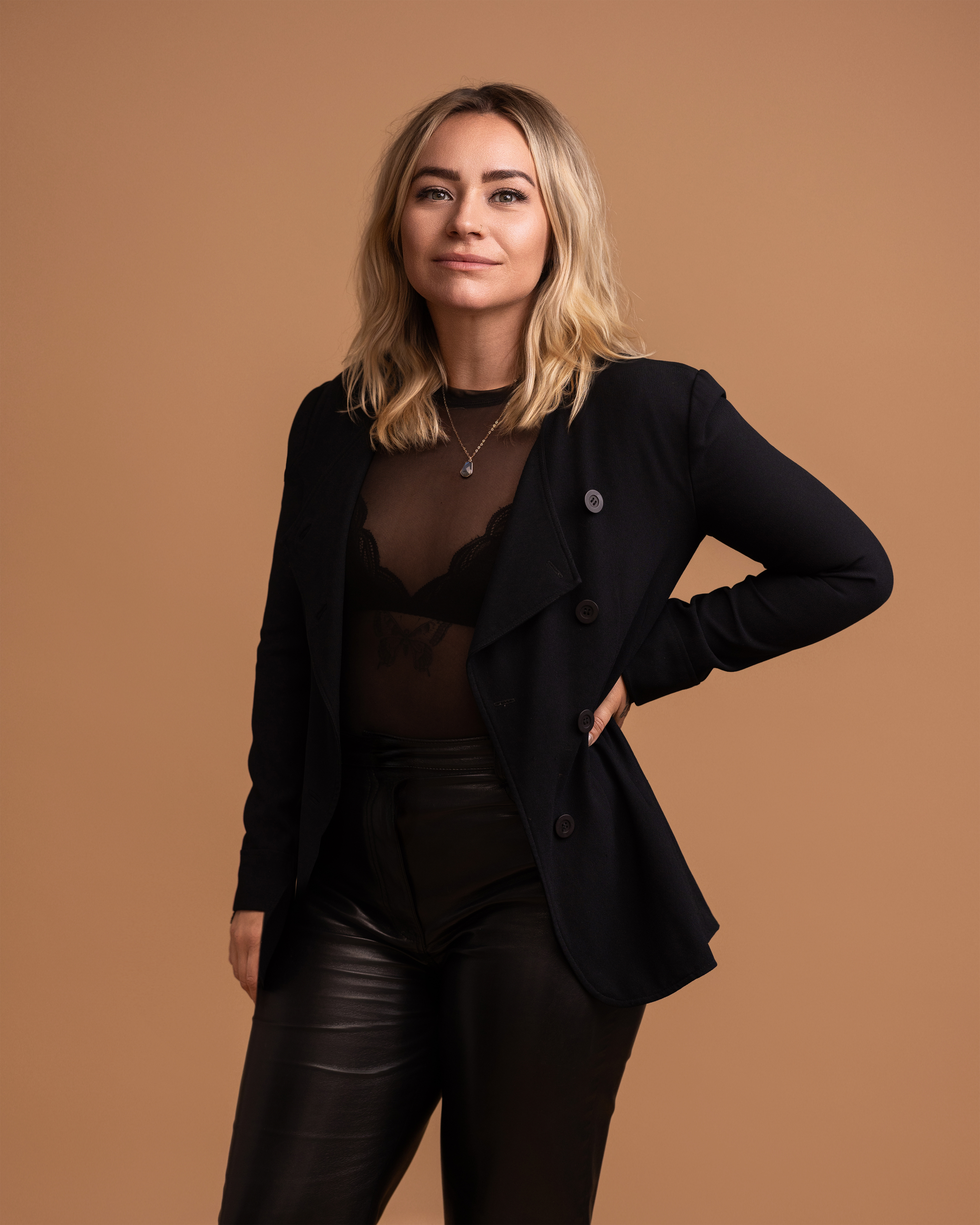 Woman wearing a black blazer over a sheer top on a brown background