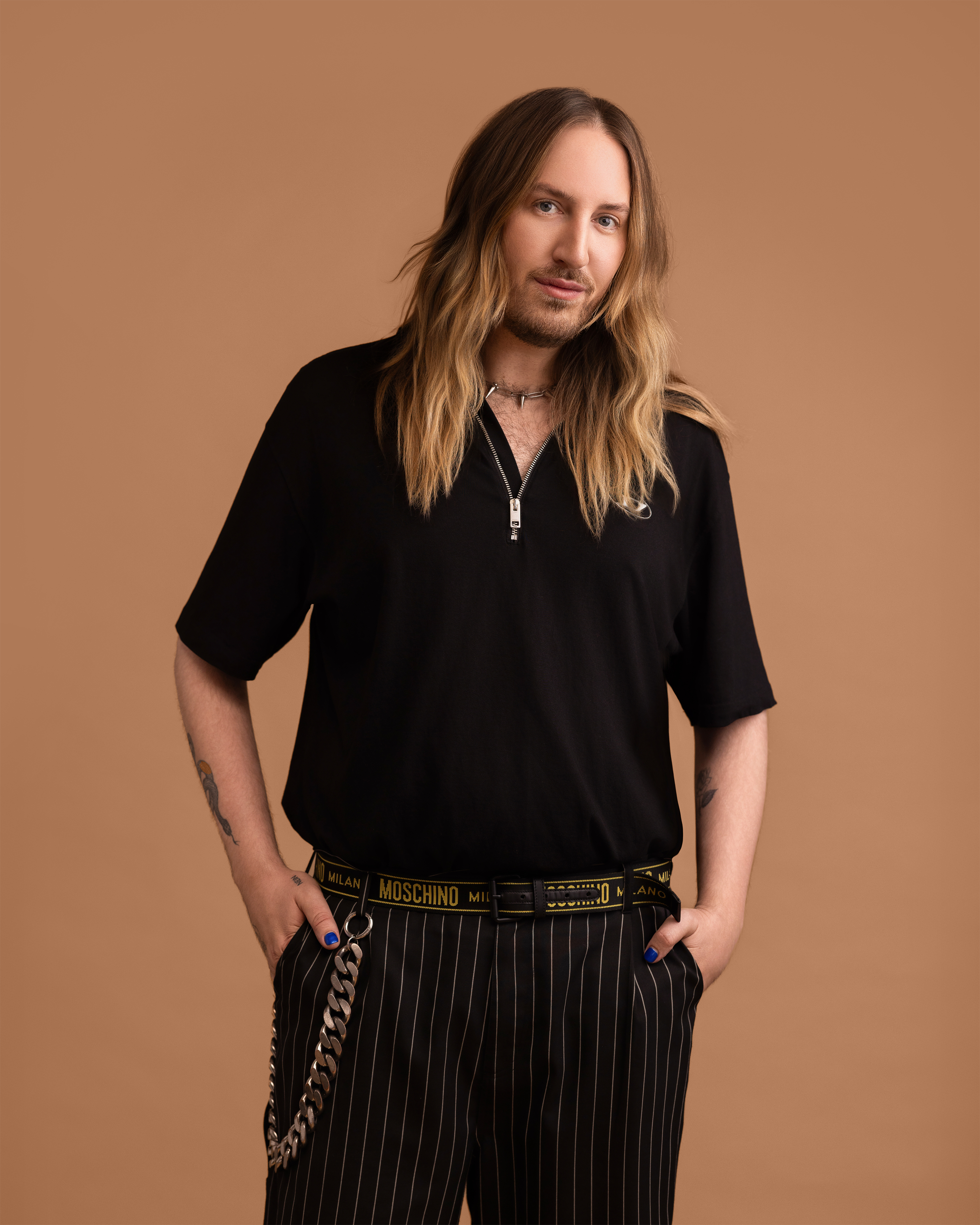 Man wearing a black shirt and striped pants with a Moschino belt on a brown background