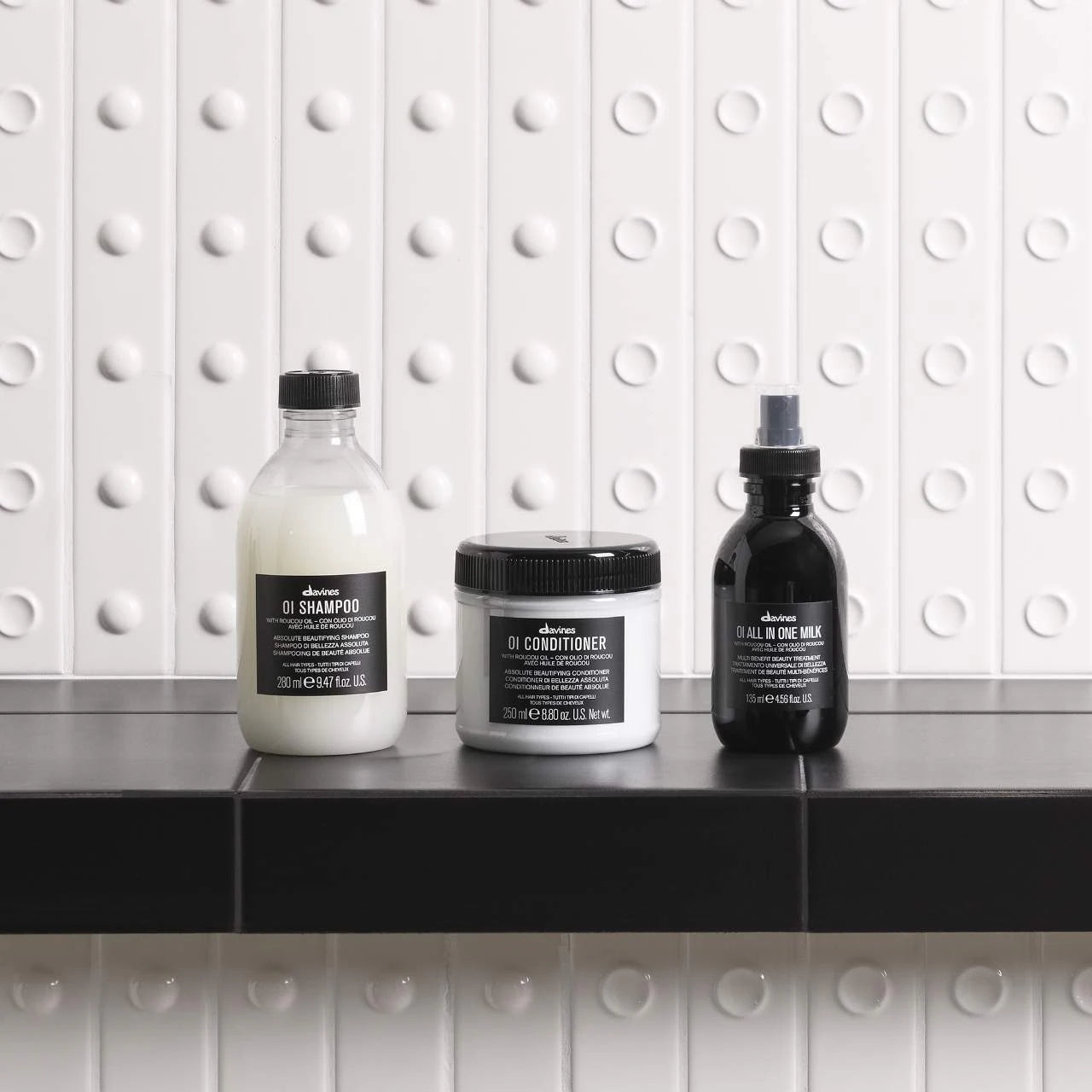 Three Davines hair care products on a black surface with a white tiled wall background