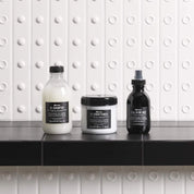 Three Davines hair care products on a black surface with a white tiled wall background