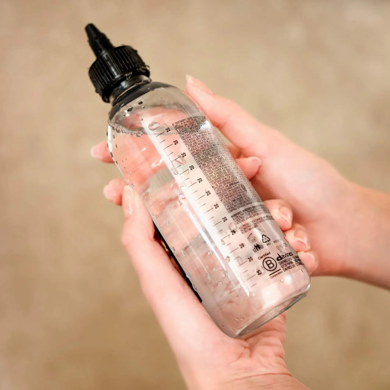 Hand holding a bottle of oi liquid luster against a beige background