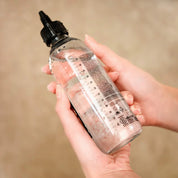 Hand holding a bottle of oi liquid luster against a beige background
