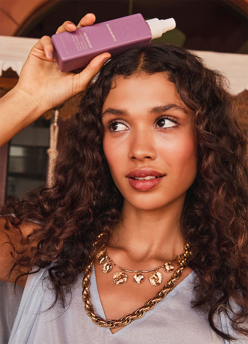 Model with curly hair holding bottle of kevin murphy untangled product