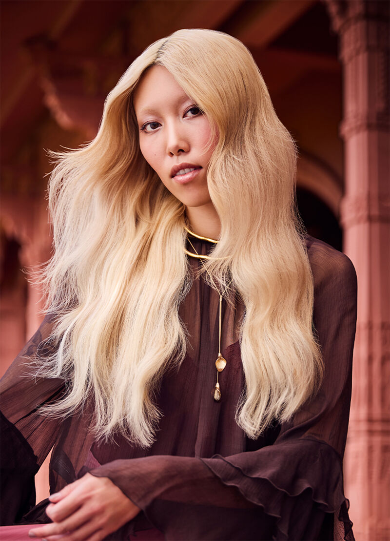 Person with long blonde hair wearing a dark outfit indoors.