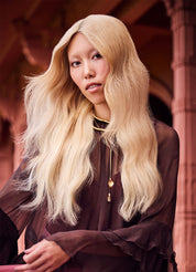 Person with long blonde hair wearing a dark outfit indoors.