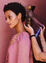 Woman applying hair product to her hair against a pink wall