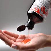 Bottle of shampoo being poured into a hand with a gray background