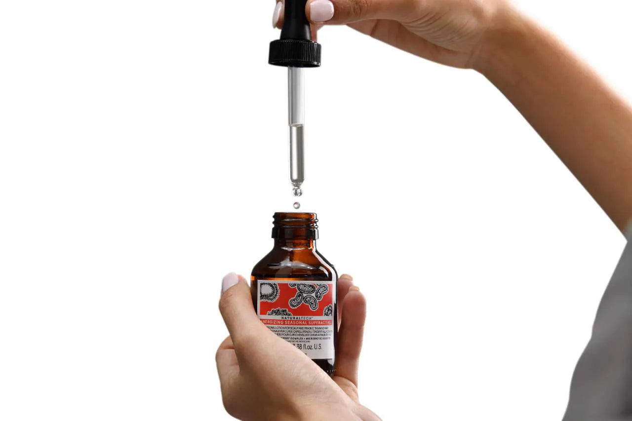 Hand holding a brown bottle with a dropper labeled seasonal superactive against a white background