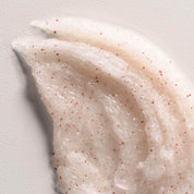 Close-up of a smooth, beige-colored cream with small red specks on a light gray background