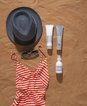 Sun hat, sunglasses, striped swimsuit, and sunscreen bottles on sand