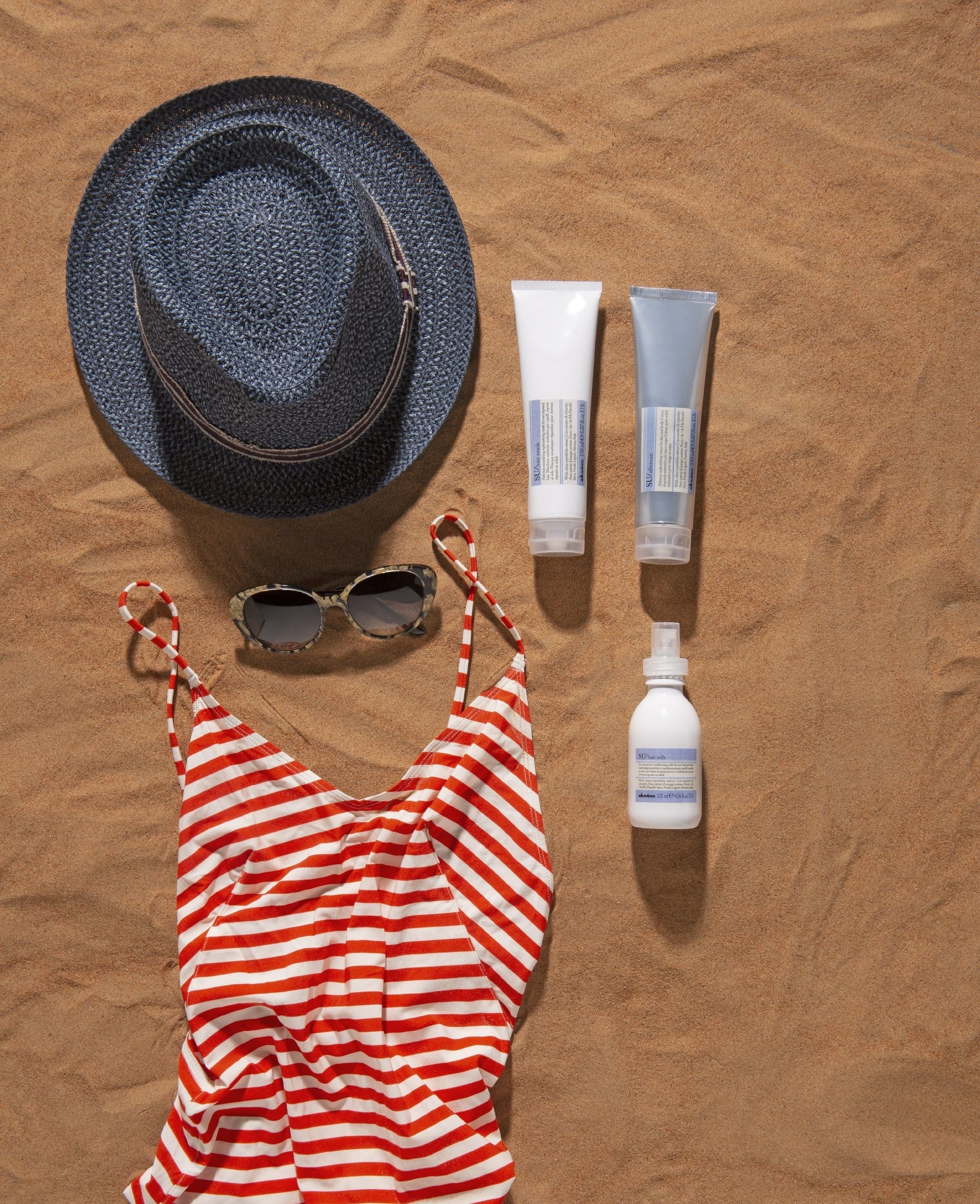 Sun hat, sunglasses, striped swimsuit, and sunscreen bottles on sand