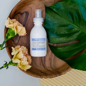White bottle with blue label on a wooden tray with flowers and leaves