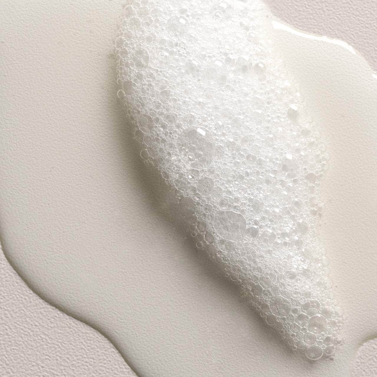 Close-up of a white, creamy product foam on a light gray background