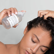 Person applying a hair product to their hair with a bottle labeled 'volu'.