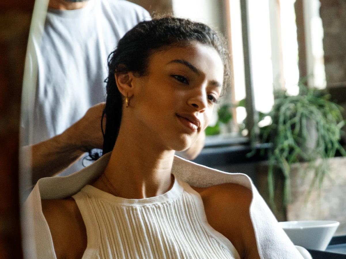 Woman in a white dress sitting in a sunlit room with plants in the background